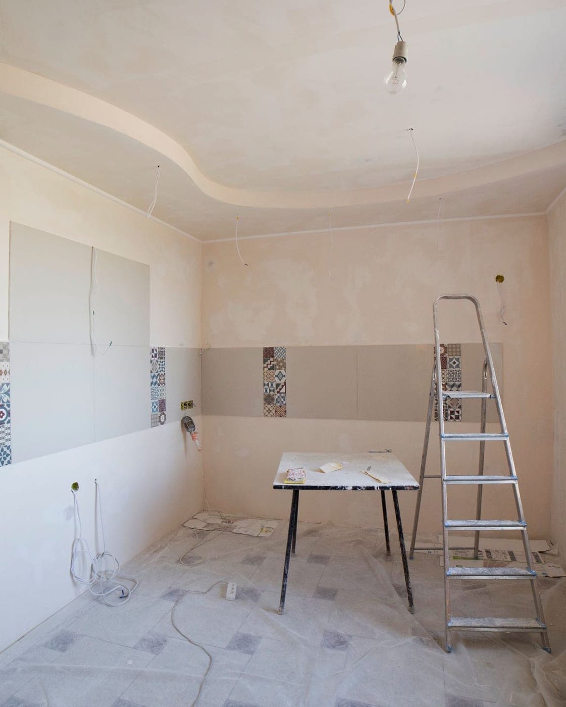 Pièce en travaux aux murs enduits, escabeau et table de chantier sur un sol couvert