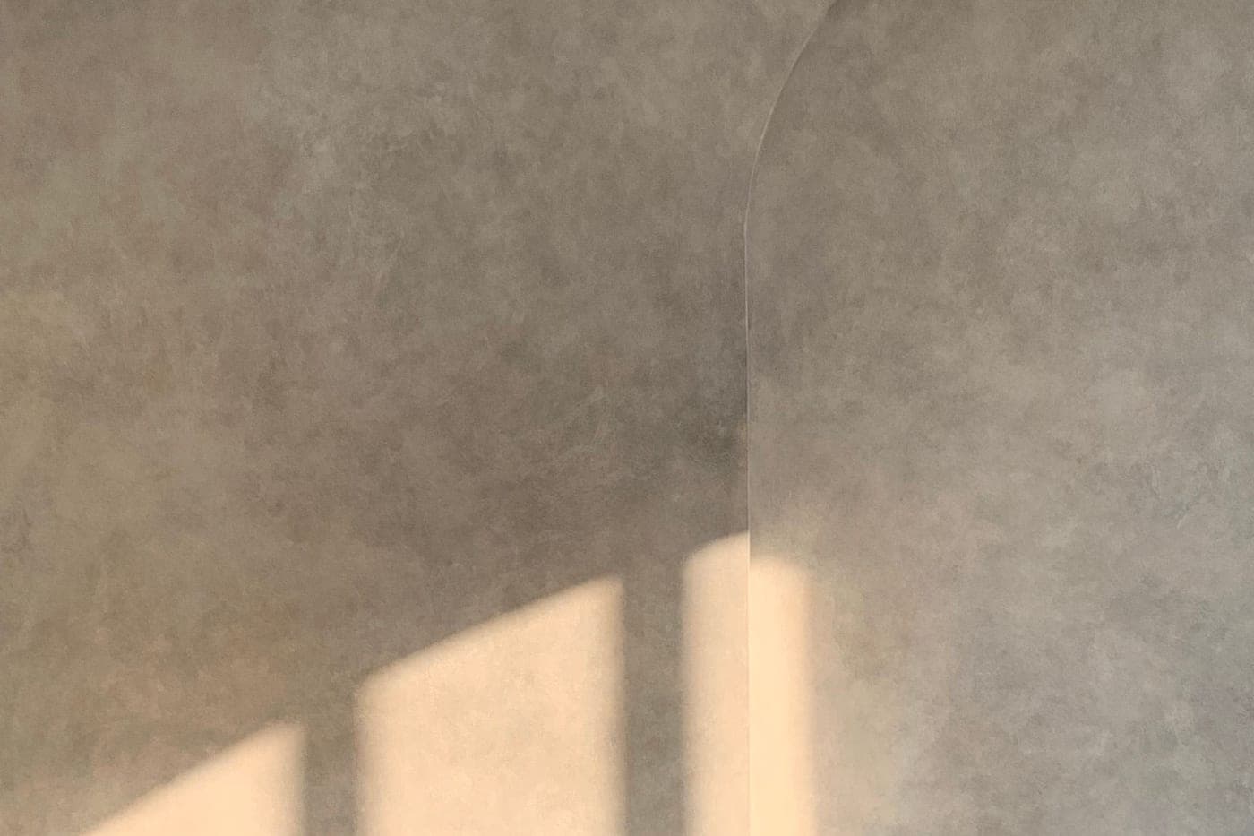 Mur enduit gris clair aux nuances douces, un rayon de lumière en travers