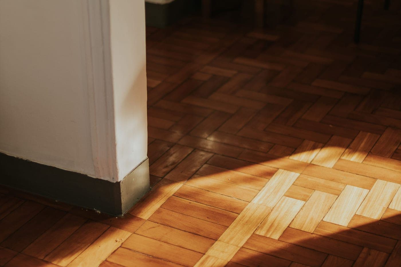 Parquet en chevrons au pied d'un mur blanc, éclairé par un rayon de soleil