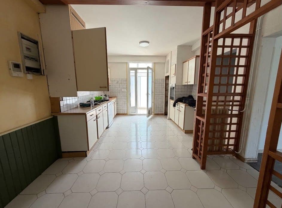 Cuisine en longueur aux meubles crème, plan de travail en bois et faïence blanche, une porte de placard ouverte