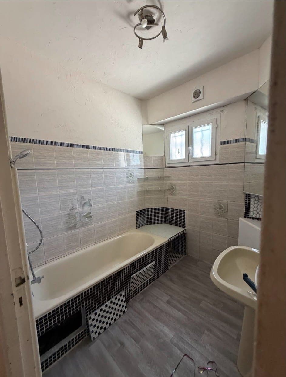 Salle de bain beige à baignoire, tablier en mosaïque noire et blanche, deux trappes déposées au sol