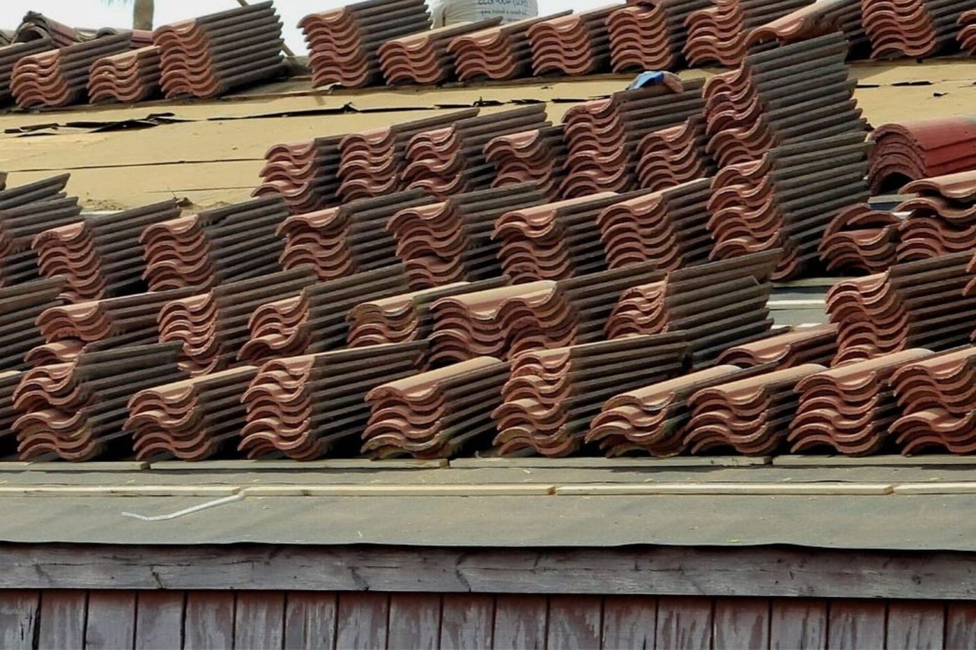 Rangées de tuiles neuves empilées sur les liteaux d'un pan de toit en cours de pose