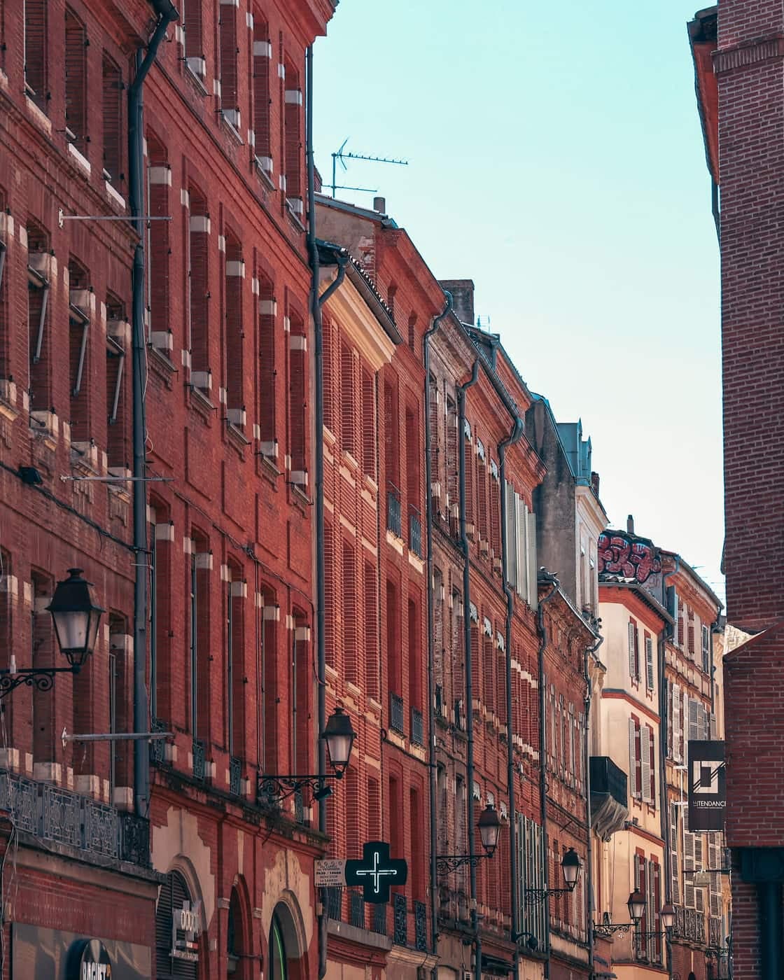 Rue de Toulouse bordée de façades en brique rose, un lampadaire en façade